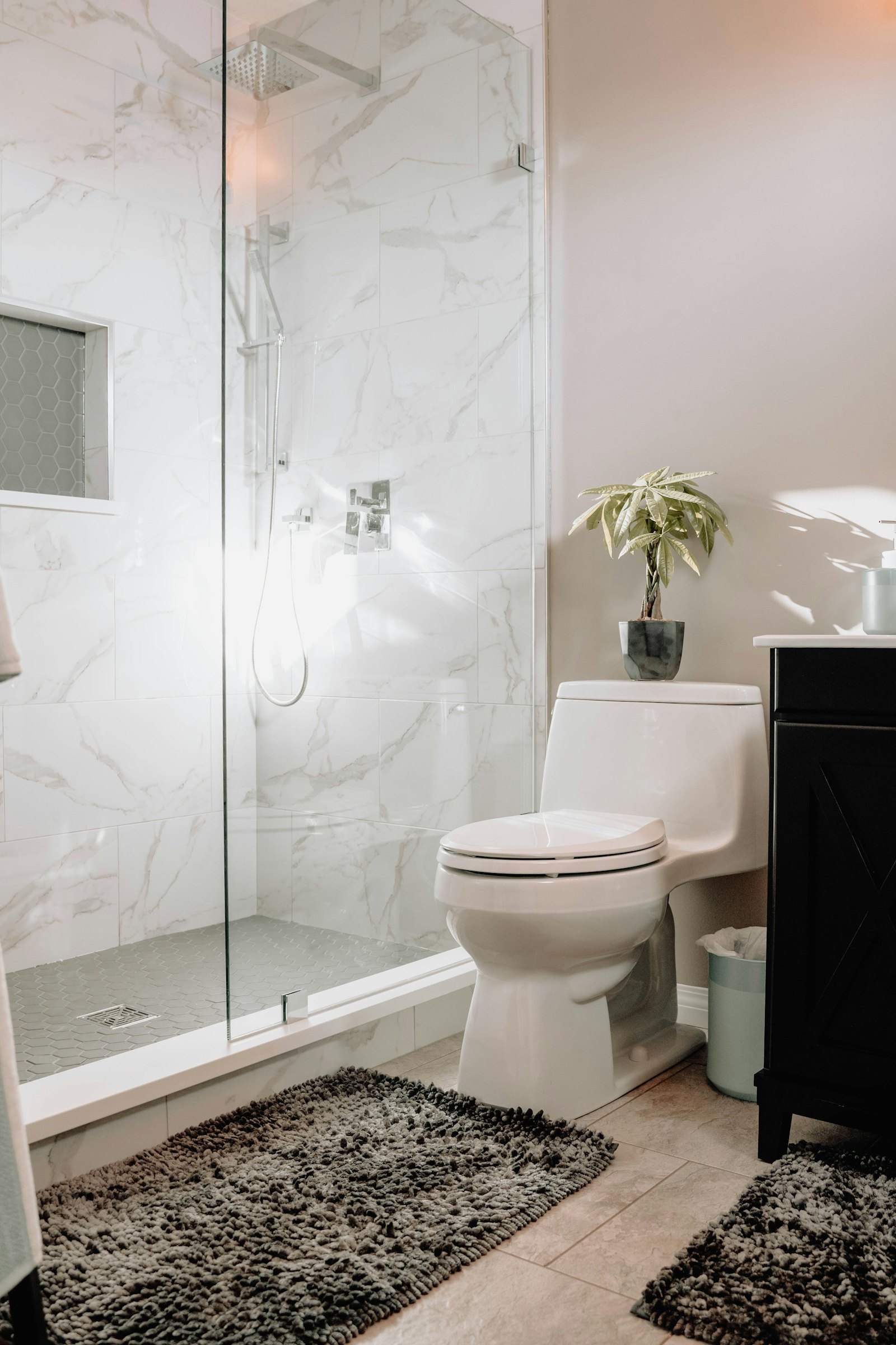 Glass shower with large marble-look tiles beside a toilet